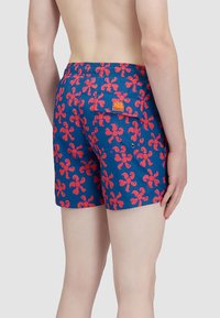 Pantaloni da bagno di colore blu navy con un motivo floreale rosso. Vita elasticizzata con tasca a patch sul retro. Tessuto morbido al tatto.