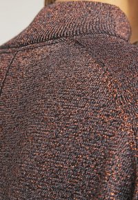 Close-up of brown and copper metallic knit fabric on a high-collar sweater worn on a person's shoulder.