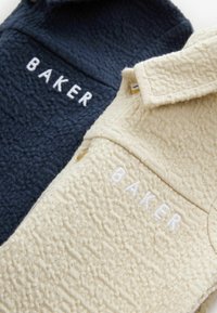 Zwei Hemden mit Kragen in Navy und Creme. Beide haben einen strukturierten Stoff mit dem Wort "BAKER" in Weiß gestickt.