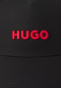 Svart caps med buet skjerm som har rød brodert "HUGO" tekst foran. Laget av glatt stoff med strukturert passform.