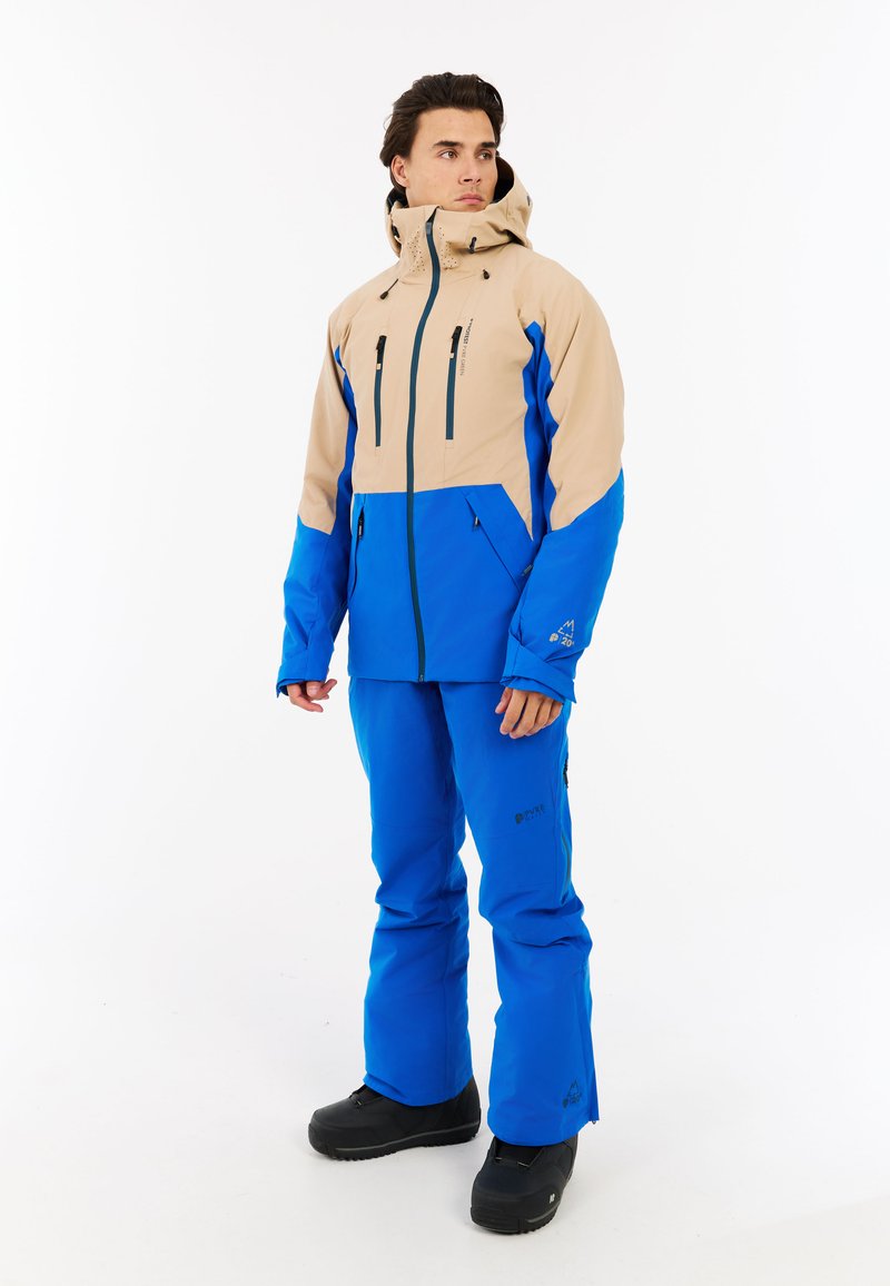 Sniego striukė ir kelnių rinkinys smėlio ir mėlynos spalvos. Striukė turi kelis užtrauktuku uždarytus kišenes, gobtuvą ir elastingus rankogalius. Medžiaga atrodo nepralaidi vandeniui.