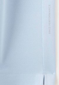 Tissu texturé bleu clair avec une couture verticale et le texte « KING PERFORMANCE » imprimé près de la couture sur le côté droit.
