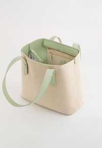 Bolso de lona en beige claro con acentos en verde menta. Cuenta con asas resistentes, bolsillo interior con cremallera y textura suave. Diseño de apertura superior.