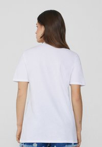 Camiseta de algodón blanca con mangas cortas, cuello redondo y un corte relajado. La vista trasera muestra una textura suave y sin gráficos visibles.