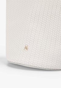 Bolso blanco texturizado con un pequeño emblema de calavera y huesos cruzados dorado cerca del centro inferior sobre un fondo liso.