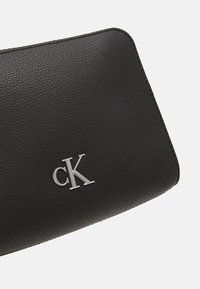 Portafoglio in pelle nera con finitura testurizzata, caratterizzato da un logo argentato "cK" nell'angolo in basso e un design pulito e minimalista.