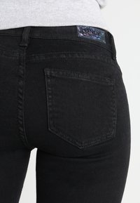 Černé denimové džíny s přiléhavým střihem, pevnými švy, viditelnou zadní kapsou a značkovou etiketou na pase.