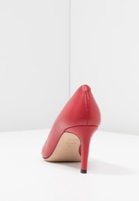 Chaussure à talon aigu en cuir rouge avec un embout pointu, un design épuré et un talon aiguille étroit. Texture lisse et accents minimalistes.
