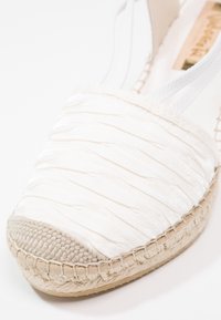 Chaussure espadrille blanche avec empeigne en tissu froncé et détail de semelle en jute tressé sur fond blanc.