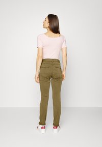 Top de manga curta rosa claro combinado com calças justas verde-azeitona. As calças têm bolsos traseiros e são estilizadas com ténis brancos.