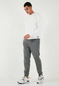 Baltas apģērbs ar apaļu kaklu, pelēkas sporta bikses un baltas kedas ar melniem akcentiem. Mīksts audums, brīvs piegriezums un ribotas aproces un potītes.