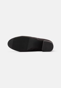 Scarpa in suede nera con punta arrotondata e tacco basso a strati. La suola è in gomma testurizzata con leggere ondulazioni per una migliore aderenza.