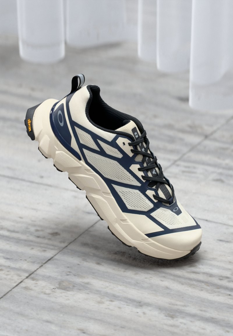 Chaussure de course légère avec une tige crème, des accents bleu marine, un mesh texturé et une semelle rembourrée ; dotée d'un talon en caoutchouc noir et d'un logo.