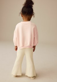 Rosa übergroßer Hoodie mit gerippten Bündchen, kombiniert mit weißen strukturierten Schlaghosen, von hinten betrachtet. Einfaches Design aus weichen Materialien.