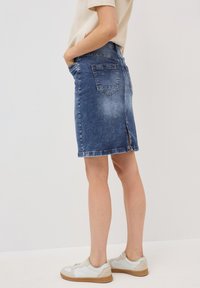 Jeanskjol i mellanblått med en blekt finish, knälång, med två bakfickor och en slits längst ner. Matchad med vita sneakers.