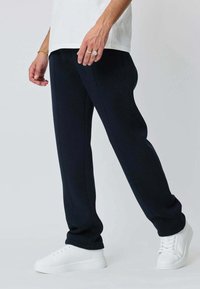 Pantalons de jogging bleu marine avec une coupe fuselée, fabriqués en tissu doux, dotés de poches latérales et terminés par des poignets côtelés. Associés à des baskets blanches.