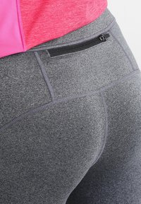 Harmaat urheiluhousut, joissa on texturoitu kangas, pieni musta vetoketjullinen tasku vyötäröllä ja kontrastiväri violetteja ompelutarkoituksia.