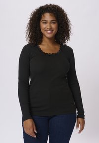 Haut noir à manches longues avec une texture côtelée, un décolleté bordé de dentelle et un petit nœud accent au centre devant, associé à un jean bleu.