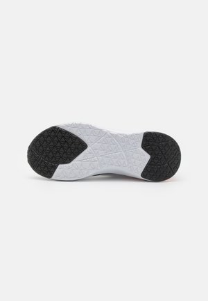 Sål på en sneaker med sort tekstureret gummi på hælen og tåen og en hvid midtersektion med geometriske mønstre.