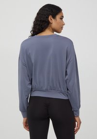 Szary, lekki sweatshirt z długimi rękawami, elastycznym dołem i luźnym krojem, połączony z czarnymi legginsami. Gładka tekstura, casualowy design.