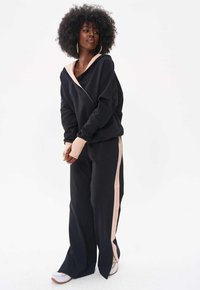 Czarna bluza z kapturem z różowym akcentem, wyróżniająca się asymetrycznym fasonem. W połączeniu z czarnymi spodniami z różowym paskiem po boku, wykonanymi z miękkiego materiału.