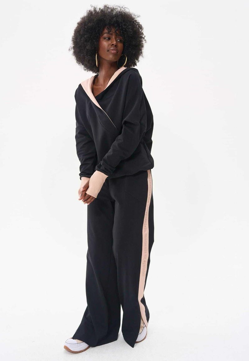 Czarna bluza z kapturem z różowym akcentem, wyróżniająca się asymetrycznym fasonem. W połączeniu z czarnymi spodniami z różowym paskiem po boku, wykonanymi z miękkiego materiału.