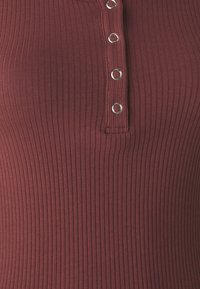 Ribbad vinröd linne med en knapplist med silverfärgade öglor. Tyget har en mjuk, elastisk textur.