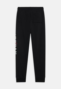 Pantalon de jogging noir avec une coupe fuselée, une taille élastique et une poche arrière unique. Présente un marquage blanc et rouge le long de la jambe gauche.