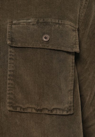 Camisa de veludo corduroy verde-azeitona com um bolso no peito com fecho de botão e um padrão texturizado em nervuras ao longo do tecido.