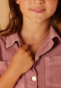 Zilveren halsketting met vijf gekleurde edelstenen (paars, roze) aan een delicate ketting. Draag het over een lichtroze corduroy overhemd met knoopdetails.