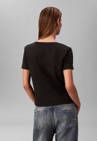 T-shirt nera a maniche corte con scollo rotondo, abbinata a jeans di denim blu slavato. Il tessuto appare morbido e casual.