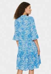 Robe à motif bleu et blanc avec des manches courtes, une silhouette évasée et un design à volants. Tissu léger avec une finition texturée.