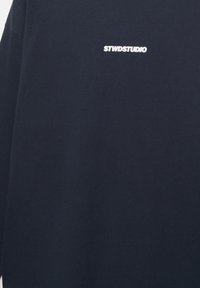 Maglietta a maniche lunghe blu navy con testo bianco "STWDSTUDIO" centrato sulla parte superiore del petto.