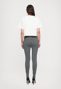 White cropped t-shirt with short sleeves paired with fitted black leggings featuring a repeated grey "MK" pattern. High heels complete the look.