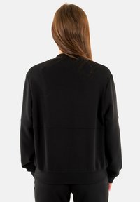 Sudadera negra confeccionada con tela suave, que presenta un ajuste relajado, cuello redondo y puños acanalados. Vista trasera que muestra una textura lisa sin adornos.