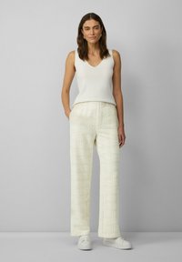 Witte mouwloze v-hals top gecombineerd met crèmekleurige geruite wijde broek en witte sneakers. Eenvoudige, gestructureerde stof met een ontspannen silhouet.