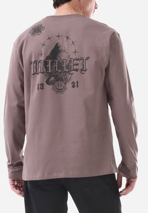 Man wearing mauve long-sleeve shirt with black graphic of mountain, stars, and text "BULLET 1921" on the back.