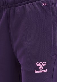 Paarse sportbroek van gladde stof, met een roze logo en de letters "XK" op de zijkant, voorzien van een elastische tailleband.