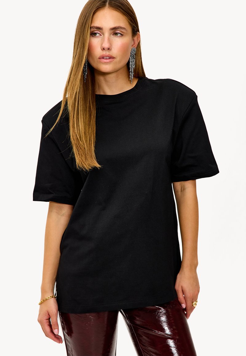 Zwarte oversized t-shirt met korte mouwen, ronde halslijn en een zachte katoenen textuur. Gecombineerd met glanzende bordeauxrode broek.