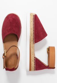Espadrilles en suède rouge avec une bride de cheville en cuir marron, semelle en caoutchouc blanc et détail en jute tressé le long du bord. Design à bout fermé.