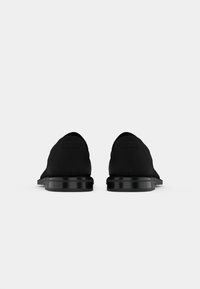 Svarta slip-on skor med ett slätt tygöverdrag, låg profil och en glansig svart sula. Minimalistisk design utan ytterligare dekorationer.