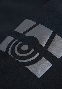 Svart tyg med en glänsande silverlogotyp som har ett abstrakt mönster och koncentriska cirklar, vilket skapar en modern visuell effekt.