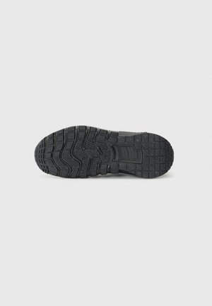 Semelle d’une chaussure de sport noire avec des motifs de bande de roulement texturés et de petites taches blanches sur la surface, présentée sur un fond clair.