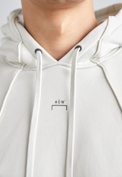 Hanorac gri deschis cu șireturi, având un mic logo imprimat pe piept, fabricat dintr-un material moale cu o textură netedă.