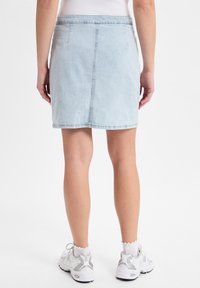 Hellblaue Jeans-Minikurze mit schmalem Schnitt, zwei Gesäßtaschen, Saum oberhalb des Knies, kombiniert mit weißen Sneakers.