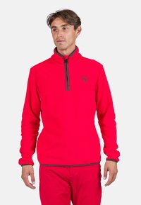 Red fleece pullover with high collar and half-zip closure. Features gray accents along zipper and cuffs. Logo on chest area.