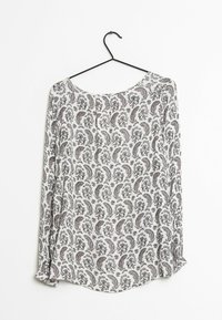 Langärmlige Bluse an einem Kleiderbügel, aus einem weißen Stoff mit aufwendigen schwarzen und roten Paisleymustern, rundem Ausschnitt und abgerundetem Saum.