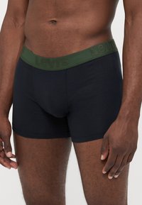 Boxers de algodão pretos com uma cintura elástica verde e a marca "Levi's" em relevo. Design ajustado com uma textura suave.