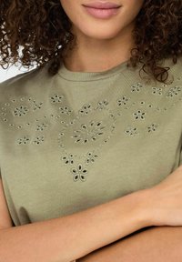 Olivengrøn bomulds T-shirt med blomsterbroderede detaljer i lysere grøn, korte ærmer og rund halsudskæring.