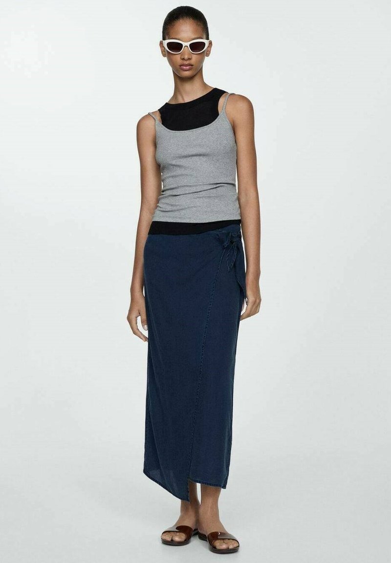 Un débardeur gris associé à une jupe portefeuille navy avec un accent à nouer. La tenue est complétée par des sandales marron et des lunettes de soleil blanches.